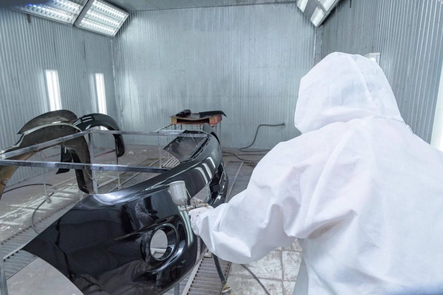 Detailer in a spray booth working on a bumper prepared for paint protection film installation